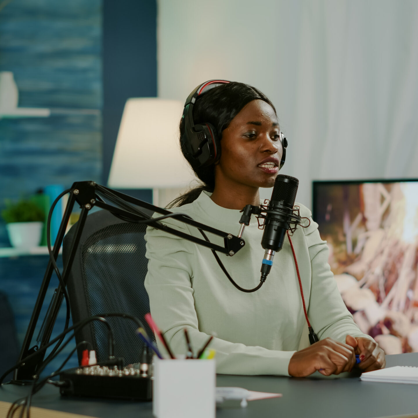 Black woman host of online show looking in laptop talking in podcast microphone with listeners entertainment. Speaking during livestreaming, blogger discussing in vlog wearing headphones.